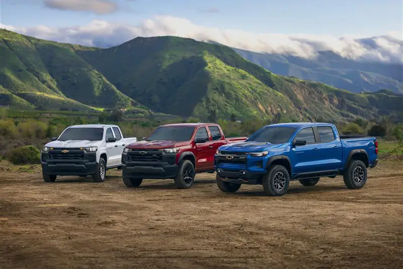 Three 2026 Chevrolet Colorado pickup trucks parked off-road with mountains in the background.
