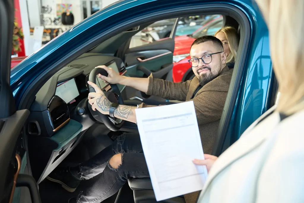 Man sitting in a new car during a dealership visit, reviewing paperwork related to Invoice Price vs. MSRP.