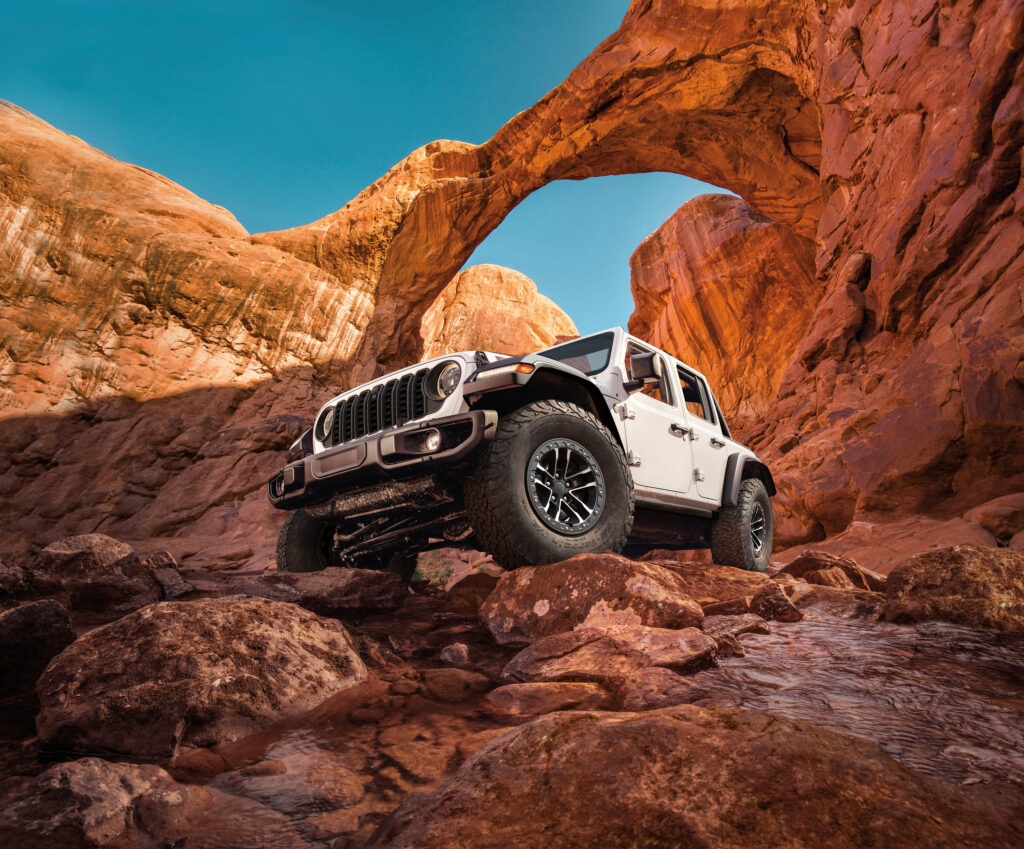 White 2026 Jeep Wrangler climbing over rocks in a desert canyon landscape