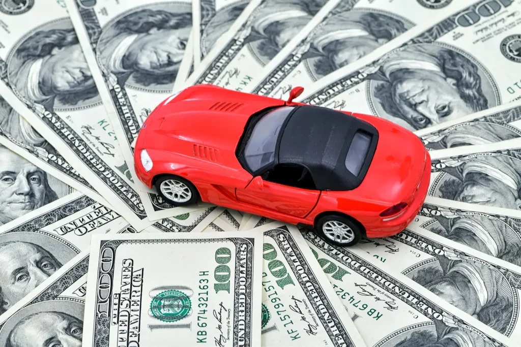 Red toy car on hundred dollar bills representing costly invoice car price lookup mistakes