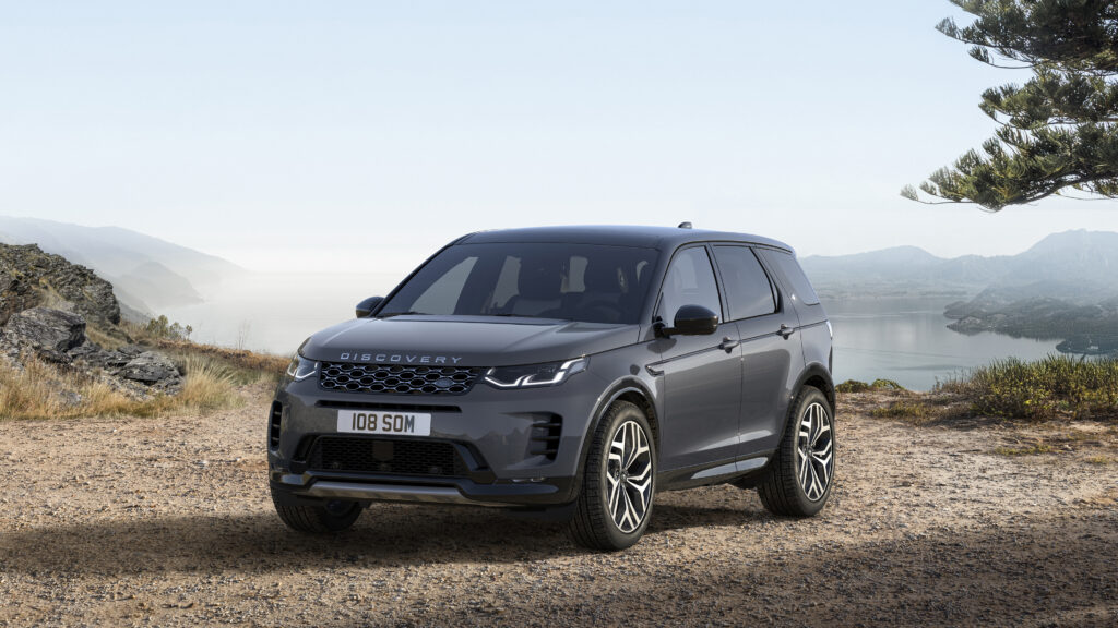 Gray Land Rover Discovery SUV parked on a gravel overlook with mountains and a lake in the background for a Land Rover Discovery Review.