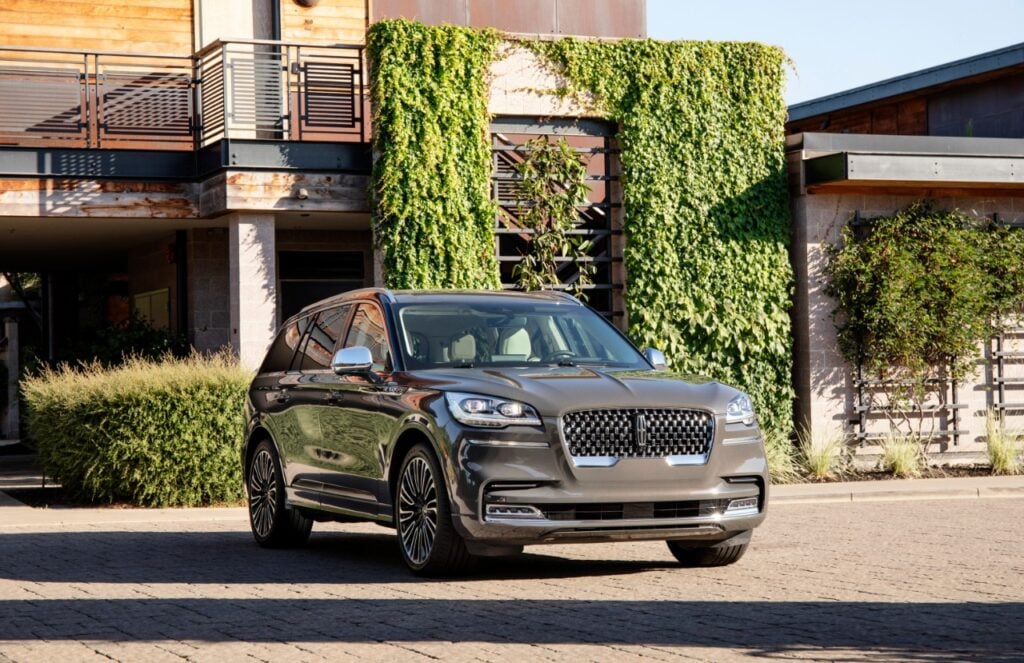 Gray Lincoln Aviator luxury SUV parked outside a modern home with greenery in the background for a Lincoln Aviator Review.