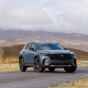 Gray Mazda CX-50 SUV parked on a winding road with mountains and cloudy skies in the background for a Mazda CX-50 Review.