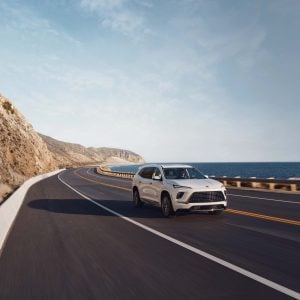 White Buick Enclave driving along a coastal highway beside the ocean, featured in our Buick Enclave Review.