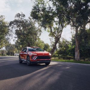 Red Buick Envision driving on a tree-lined road in daylight, featured in our Buick Envision Review.