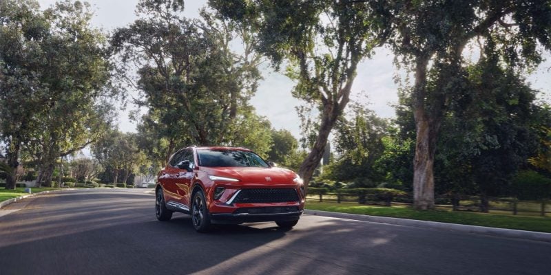 Red Buick Envision driving on a tree-lined road in daylight, featured in our Buick Envision Review.