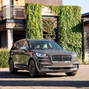 Gray Lincoln Aviator luxury SUV parked outside a modern home with greenery in the background for a Lincoln Aviator Review.