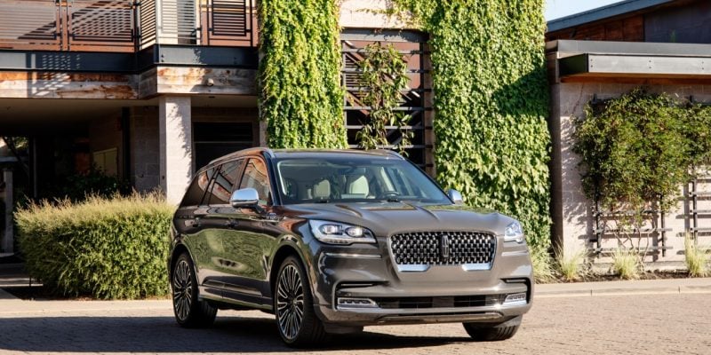 Gray Lincoln Aviator luxury SUV parked outside a modern home with greenery in the background for a Lincoln Aviator Review.