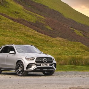 Silver Mercedes-Benz GLE luxury SUV parked in front of green hills and open countryside for a Mercedes-Benz GLE Review.