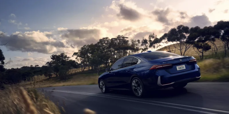 A blue BMW 5 Series driving on a two-lane road at sunset, shown in our BMW 5 Series Review.