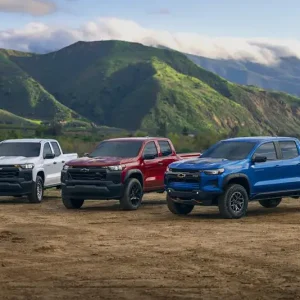 Three 2026 Chevrolet Colorado pickup trucks parked off-road with mountains in the background.