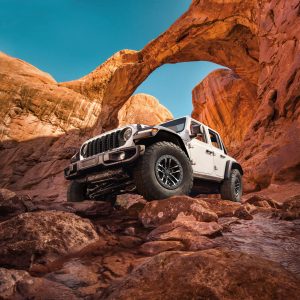 White 2026 Jeep Wrangler climbing over rocks in a desert canyon landscape