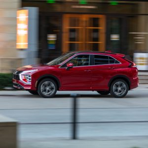 Red Mitsubishi Eclipse Cross driving through a city street in side profile for a Mitsubishi Eclipse Cross Review.