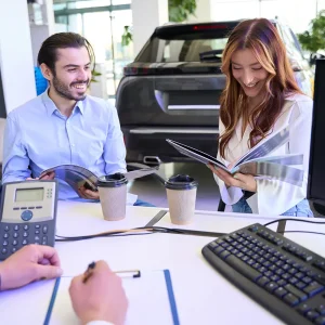Couple reviewing vehicle pricing information with a salesperson at a car dealership