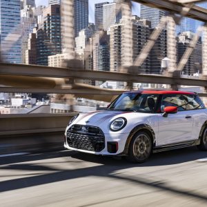 White MINI Cooper 2 Door driving across a city bridge with a skyline in the background for a MINI Cooper 2 Door Review.