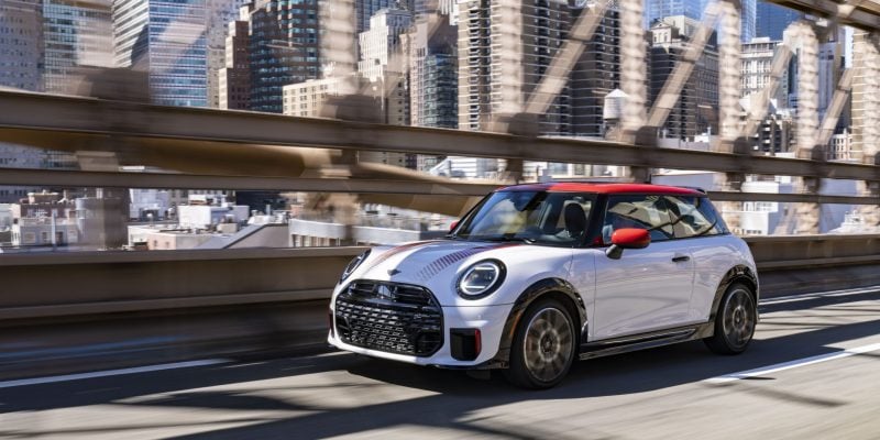 White MINI Cooper 2 Door driving across a city bridge with a skyline in the background for a MINI Cooper 2 Door Review.